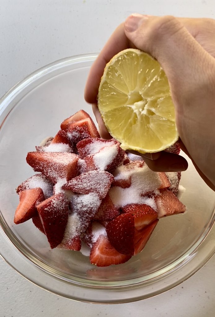 Adding sugar and lemon juice to fresh strawberries to serve with the basil olive oil cake.