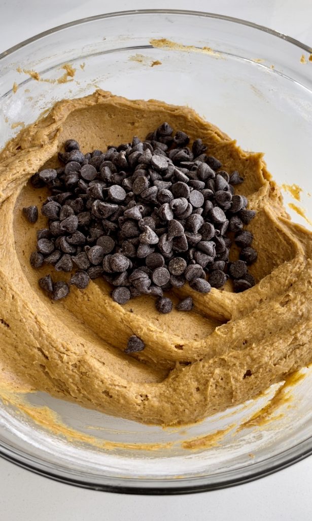 Adding chocolate chips to pumpkin flavored cookie cake batter.