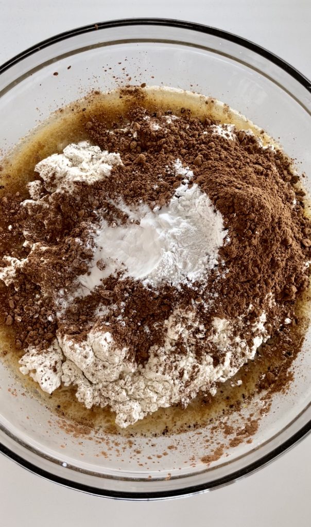 Mixing the flour, cocoa powder, baking powder and baking soda into the wet ingredients to form a batter for chocolate cake with peanut butter frosting.